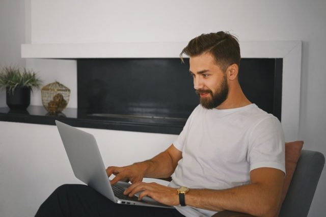 Top activități online pentru serile de vară: de la streaming la experiențe interactive gratuite stylish bearded young male relaxing at home with portable comput