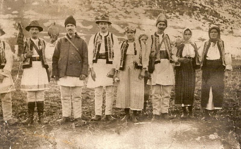 Oameni în costum tradițional românesc, în natură, pentru o fotografie veche.
