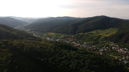 Vedere panoramică a zonei Almaș-Dobreni cu munți și sat.
