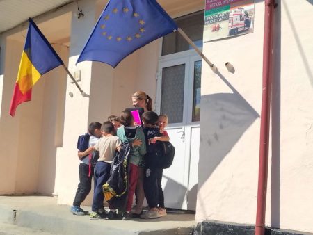 Grup de elevi cu drapele UE și România în fața școlii.