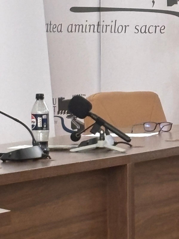 Primăria Târgu-Neamț: afară-i vopsit gardul, înăuntru, mucegai și igrasie 5 Microfon, sticlă de apă și ochelari pe masă de conferință.