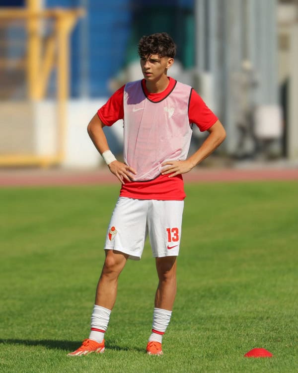 Jucător de fotbal tânăr în echipament roșu și alb pe teren.