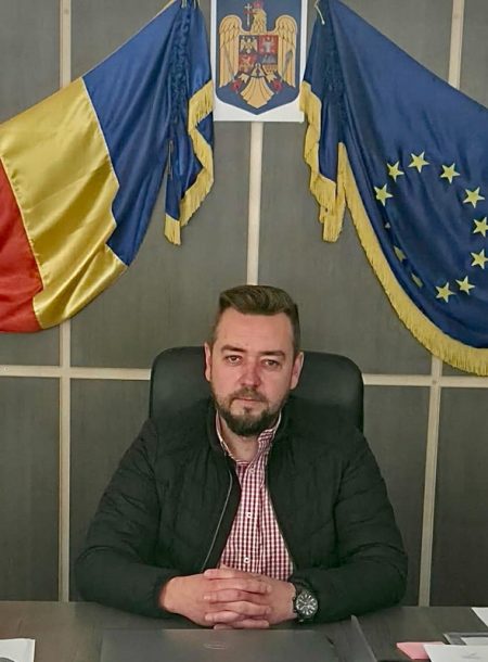 Bărbat în fața drapelelor României și UE, simbolizând investițiile locale.