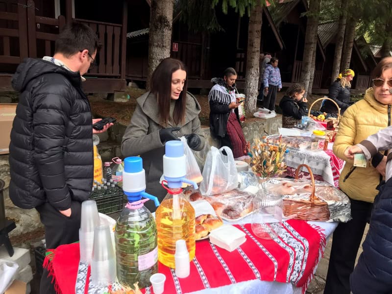 Meniu și sticle pe masă la tarabă cu oameni în fundal.