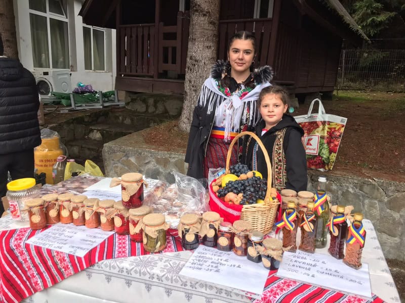 Tineri de etnie romă vând produse tradiționale turta cu miere și gem la un tarabă într-un târg.