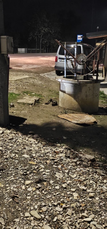 Duză lângă un monument metalic pe un teren pietruit, noaptea.