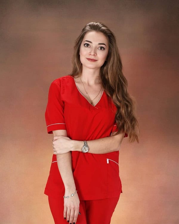 Alexandra Cumpănici în uniformă medicală roșie, zâmbind în studio.