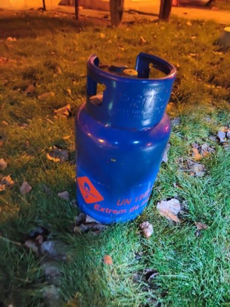Recipient de gaz albastru pe iarbă lângă trotuar, noaptea.