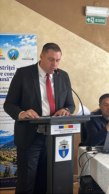 Bărbat în costum la microfon, vorbind la eveniment despre comunitățile montane.