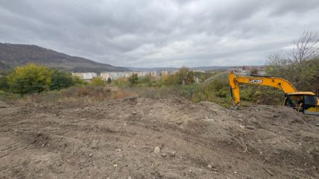 Șantier de construcții în teren arid cu excavator galben în partea dreaptă.