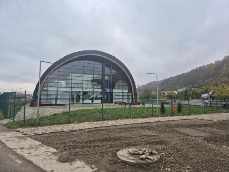 Foto. Un părinte anonim a făcut treaba Primăriei Târgu-Neamț Clădire arcuită modernă cu geamuri mari într-un parc, cer înnorat.