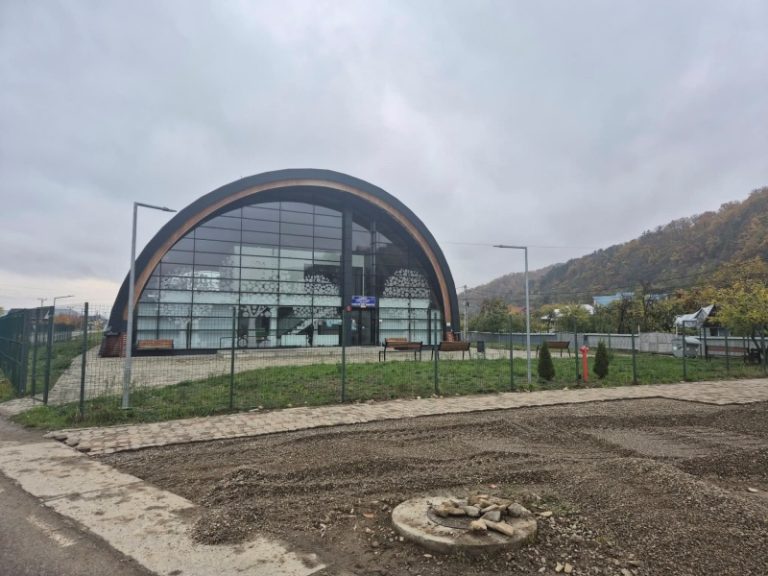 Foto. Un părinte anonim a făcut treaba Primăriei Târgu-Neamț Clădire arcuită modernă cu geamuri mari într-un parc, cer înnorat.