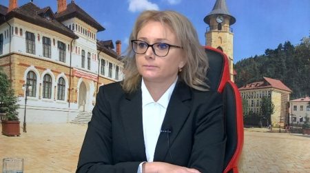 Profesionistă femeie în costum negru, prezentă într-o conferință, sediu istoric în fundal.